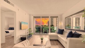 A modern living room with a sofa, coffee table, and a painting of a beach scene. - Modern Hollywood Beach Escape |  City Views (Hollywood)