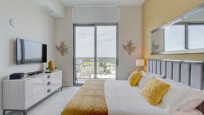 Quarto de hotel com cama, televisão, cômoda e uma grande janela com vista para a cidade.