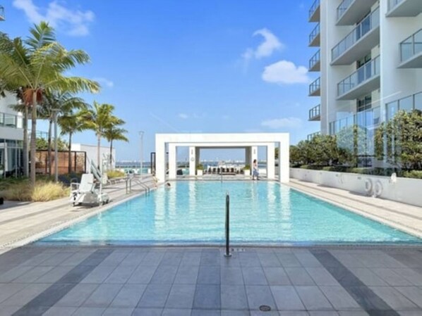 Un espace piscine moderne offrant une vue dégagée sur la piscine, un coin salon couvert et un bâtiment doté de balcons.
