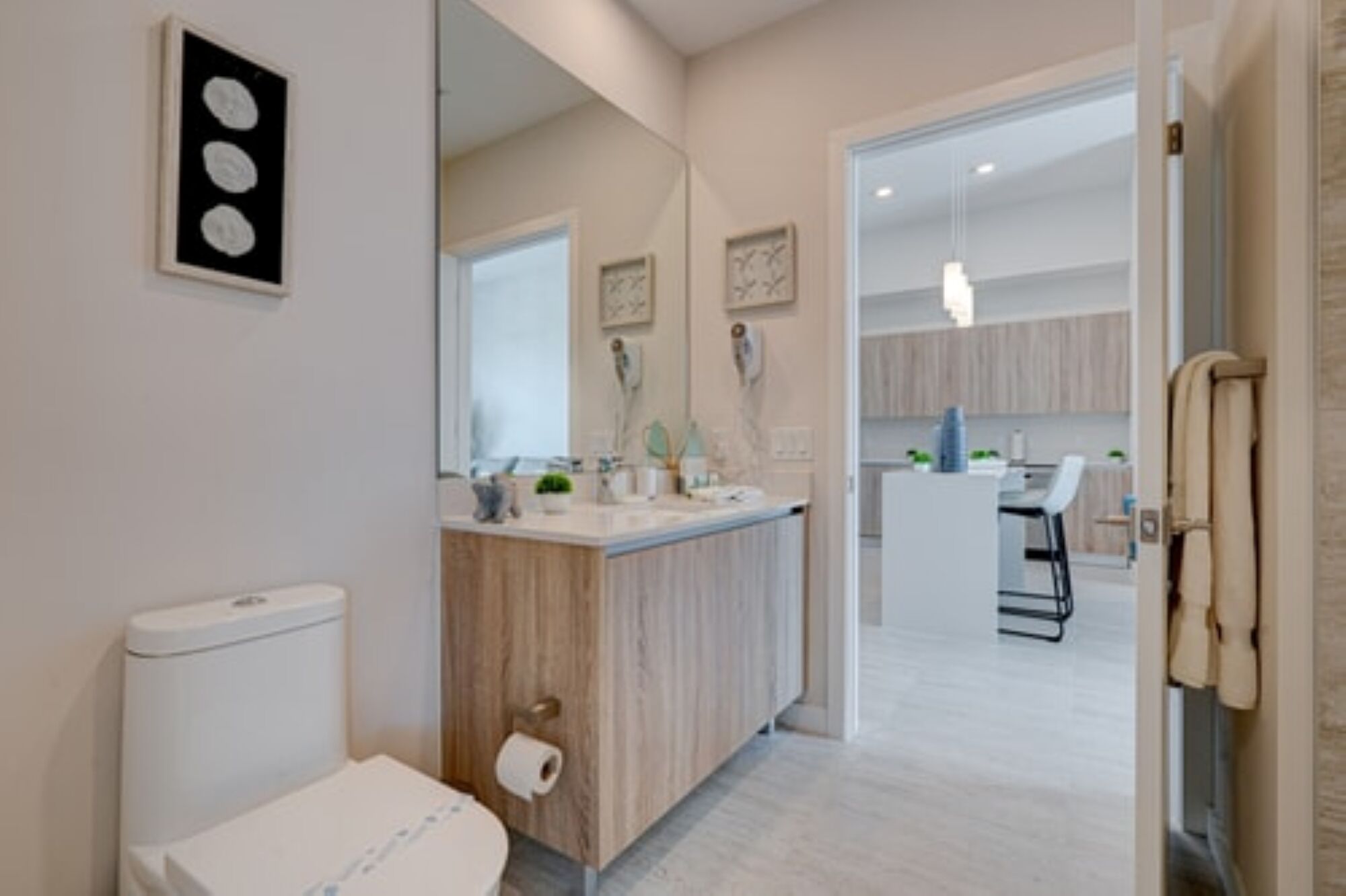A modern bathroom with a toilet, sink, and mirror. There is a hallway leading to a dining area with chairs and a table.