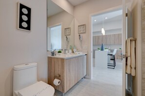 Une salle de bain moderne équipée de toilettes, d’un lavabo et d’un miroir. Un couloir mène à une salle à manger avec des chaises et une table.