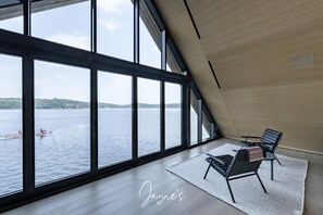 Une pièce spacieuse avec de grandes fenêtres donnant sur un lac et sur des kayaks.