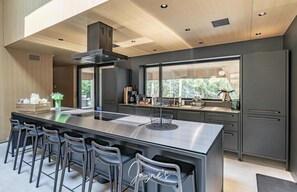 Une cuisine moderne dotée d’un grand îlot central, de tabourets de bar et offrant une vue sur la verdure environnante.