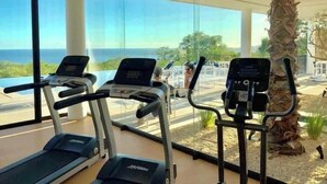 Ein Fitnessstudio mit Laufbändern und Trainingsgeräten, großen Fenstern und Meerblick.