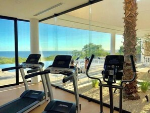 Ein Fitnessstudio mit Laufbändern und Trainingsgeräten, großen Fenstern und Meerblick.