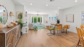 Un vaste espace de vie comprenant une table à manger, des chaises et un canapé. Un grand miroir orne le mur, ainsi qu’une plante en pot, et une fenêtre offre une vue sur l’extérieur.