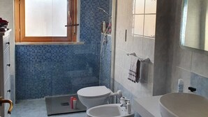 Un bany amb dues vàteres, una banyera, un lavabo i una finestra amb persianes.
