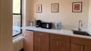 A kitchen with a window, a sink, a microwave, a kettle, and a cabinet. - Delightful 1-bedroom suit in boutique guesthouse with AC in vibrant New York (New York)
