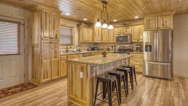 Eine Küche mit Holzausstattung, einem Edelstahlkühlschrank, einer Granit Arbeitsplatte und Barhocker.