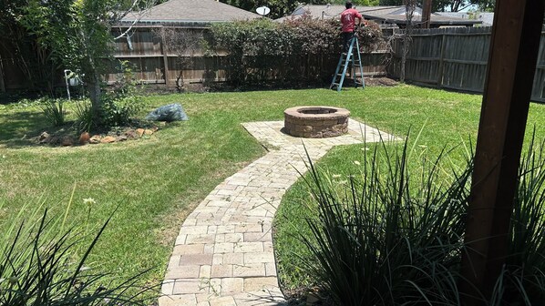 A backyard with a stone pathway leading to a fire pit, surrounded by grass and plants. - Spacious 4-bedroom house in charming Houston area. (Houston)