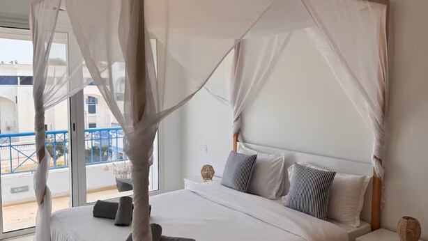 A bedroom with a canopy bed, a bedside table, a nightstand, and a view of the outside. - Gammarth Blue Pearl (La Marsa)