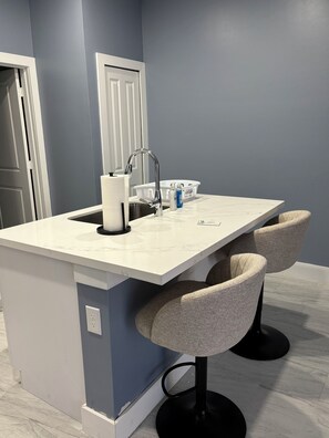 A modern kitchen with a white marble countertop, a built-in sink, and two bar stools.