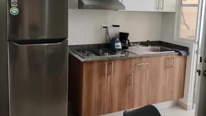 A compact kitchen with a stainless steel refrigerator, a microwave, a coffee maker, wooden cabinets, and a dining area with a table and chairs. - APARTMENT IN CANCUN WITH SWIMMING POOL IN A CONDOMINIUM (Cancún)