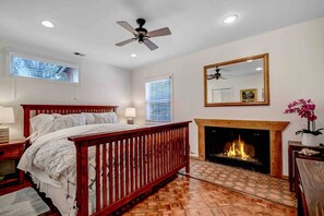 A bedroom with a bed, a fireplace, a ceiling fan, and a window with blinds. - Arches - Olive Grove Cottage (Sonoma)