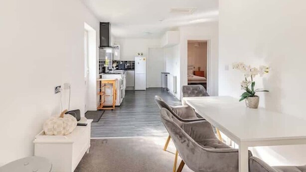 A modern kitchen with a central island, a dining area with a white table and grey chairs, and a small seating area with a white sofa.