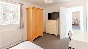 A room with a bed, a wooden wardrobe, a TV, and a desk.