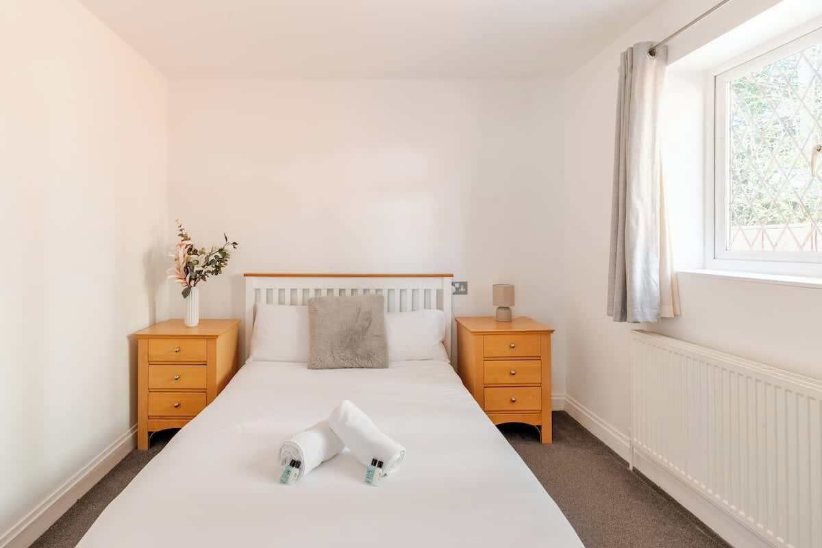 A bedroom with a bed, two nightstands, a window with curtains, and a radiator.