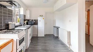 A narrow kitchen with a gas stove, white cabinets, and a refrigerator.