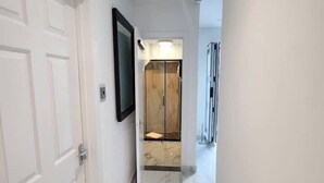 A hallway with white doors, a marble floor, and a glass elevator door.