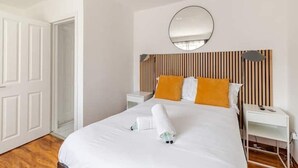 A hotel room with a bed, a bedside table, a nightstand, a mirror, and a door.
