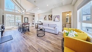 A modern living room with a sofa, yellow armchairs, a dining area, and artwork on the walls. - k211- AC, Pool/Hot Tub, Parking, BBQ, View (Canmore)