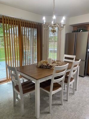 A dining area with a wooden table, white chairs, a chandelier, and a view through a window with blinds. - Charming 3-bedroom house in gorgeous Howard with AC and fitness room (Howard)