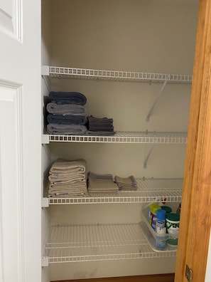 Un armario de almacenamiento con estantes que contienen toallas dobladas y un recipiente con productos de limpieza.