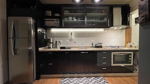 Une cuisine de taille réduite équipée d’un réfrigérateur, d’un four à micro-ondes, d’une cuisinière et de meubles de rangement aux couleurs sombres.