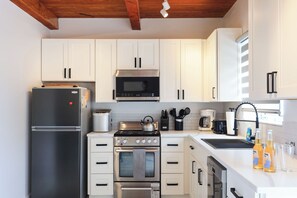 A modern kitchen with white cabinets, stainless steel appliances, and a wooden ceiling. - Caicos Calm: Serene 2BR Condo in Whitby, North Caicos - a Garden Isle Getaway (Whitby)
