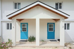 A two-story building with a white facade, two blue doors, and a small porch area. - Caicos Calm: Serene 2BR Condo in Whitby, North Caicos - a Garden Isle Getaway (Whitby)