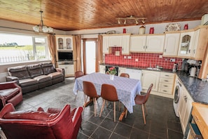 A cozy living area with a sofa, a dining table with chairs, a kitchen with red tiles, and a view through the window. - SWEETBRIAR LODGE, family friendly in Loughglynn, County Roscommon (Castlerea)