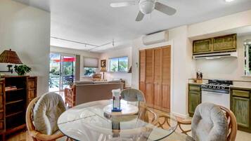 A dining area with a glass table, wicker chairs, a ceiling fan, and a kitchen with wooden cabinets and a stove.