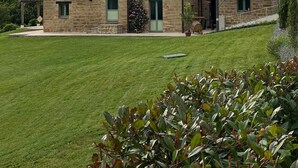 Un bâtiment en pierre doté de nombreuses fenêtres et d’un toit en tuiles, entouré d’une pelouse bien entretenue et de quelques plantes.
