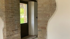 Un couloir aux murs en briques apparentes, avec une porte donnant sur l’extérieur et un sol carrelé.