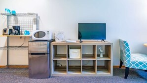 Eine kompakte Küchenzeile mit Mikrowelle, Kühlschrank und Kaffeemaschine. Ein Flachbildfernseher ist an einem Holzständer befestigt.