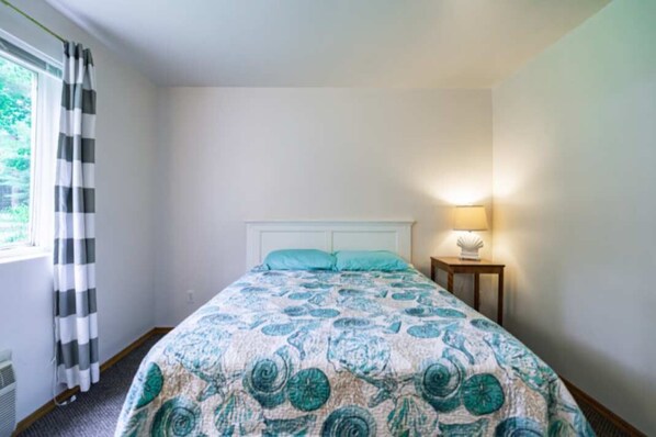 Un dormitorio con cama, mesita de noche, lámpara y ventana con cortinas.