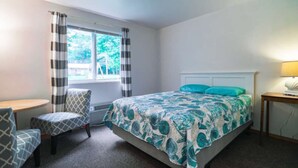 Ein Schlafzimmer mit einem Bett, einem Sessel, einem Tisch und einem Fenster mit Vorhängen.
