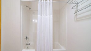 Eine Dusche mit weißem Vorhang, einem Metallregal und einer Badewanne.