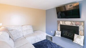 A living room with a sofa, a flat-screen TV, and a stone fireplace. - Cabin #7 Wishing Star (Iosco County)