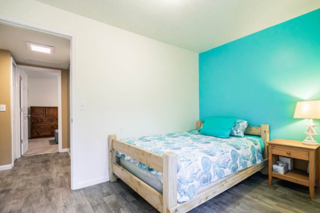 Une chambre avec un lit en bois, un mur d’accent de couleur turquoise et une table de chevet avec une lampe.