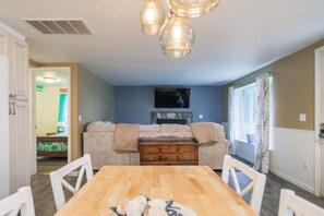 Ein Essbereich mit Holztisch und Stühlen, einer Chandelüster, einem Sofa mit Decke und einer Kommode.
