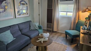 A living room with a sofa, a round coffee table with a starfish, a chair, and artwork on the wall. - Cabin #2 Water's Edge (Iosco County)