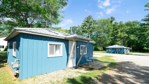 A small, single-story blue cabin with a porch, a window, and a door. - Cabin #2 Water's Edge (Iosco County)