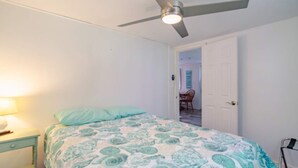 Un dormitorio con cama, ventilador de techo, mesita de noche y puerta que da a otra habitación.