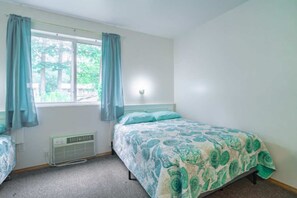 Un dormitorio con cama, ventana con cortinas, radiador e iluminación en la pared.