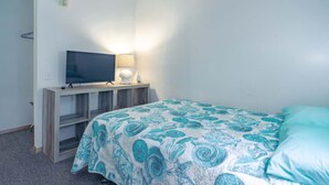 Un dormitori amb un llit, una televisió, una taula de nit i una làmpada.