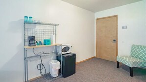 Habitació petita amb cuineta, microones, nevera, safata d'escombraries, cadira i porta.