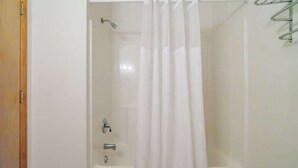 Dusche mit Vorhang, ein Metallregal und eine Badewanne.