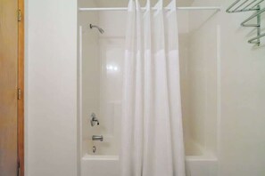Ducha con cortina, un estante metálico y una bañera.