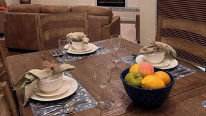 Een eetgedeelte met een houten tafel gedekt voor een maaltijd, een televisie boven de open haard en een plafondventilator.